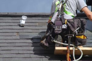 Inspector examines roof shingles beside a ladder while another person reviews notes near the house.